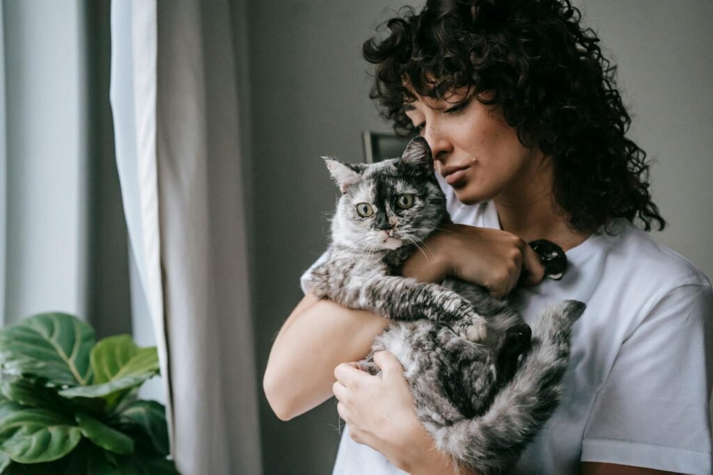A woman lovingly cuddles her gray cat by the window, capturing a serene moment indoors.