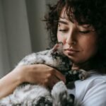 A serene moment of a woman cuddling her fluffy gray cat indoors.