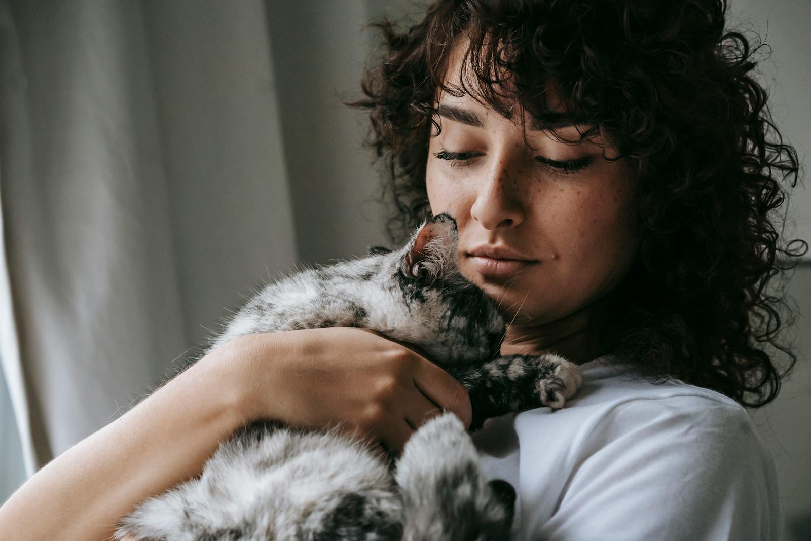 A serene moment of a woman cuddling her fluffy gray cat indoors.