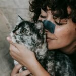 A joyful woman with curly hair cherishes her pet cat, capturing a moment of love and companionship.