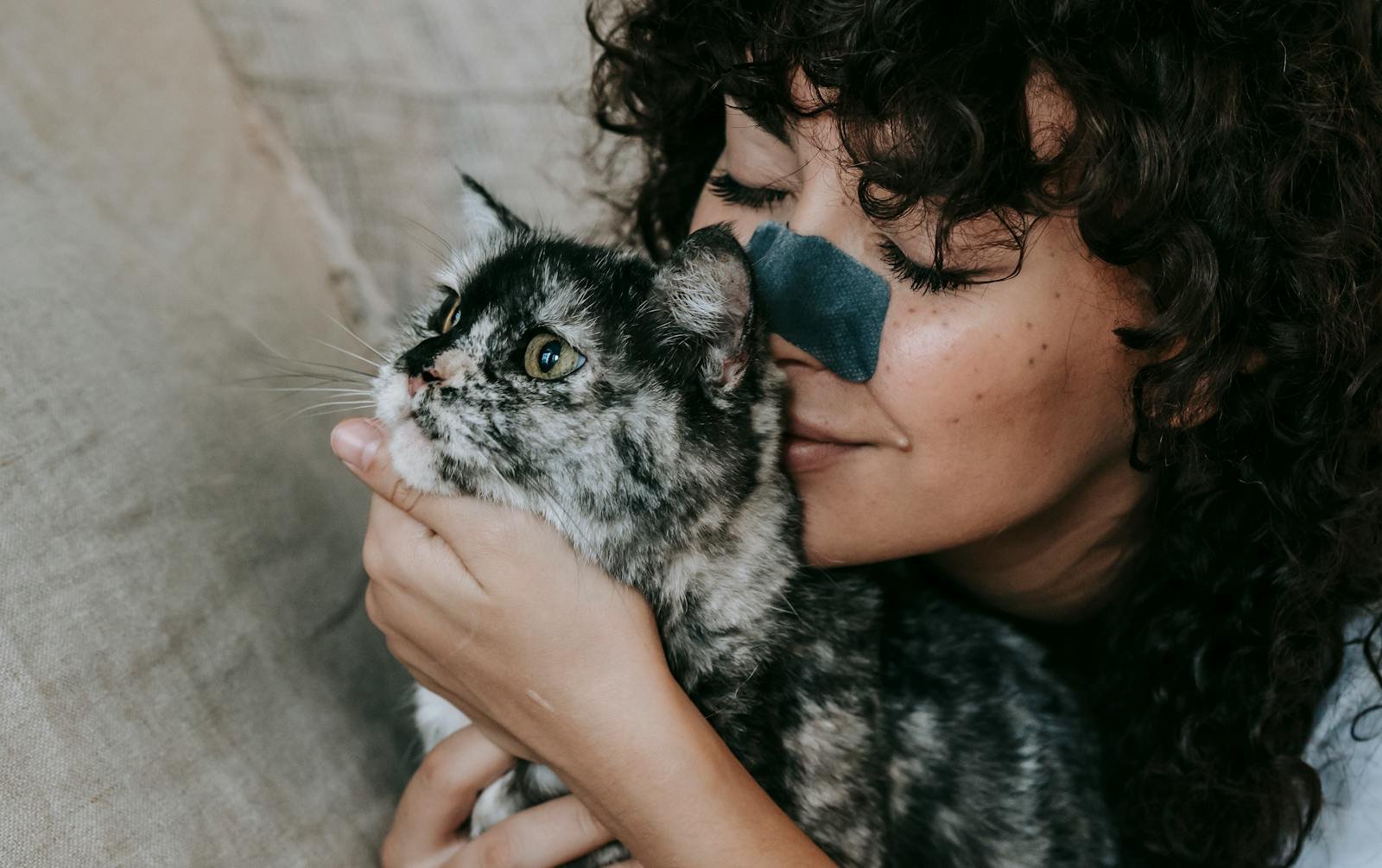 A joyful woman with curly hair cherishes her pet cat, capturing a moment of love and companionship.