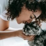 Crop content woman with curly hair caressing and touching with nose fluffy cat
