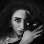 A striking black and white portrait of a woman holding a black cat, showcasing elegance and mystery.