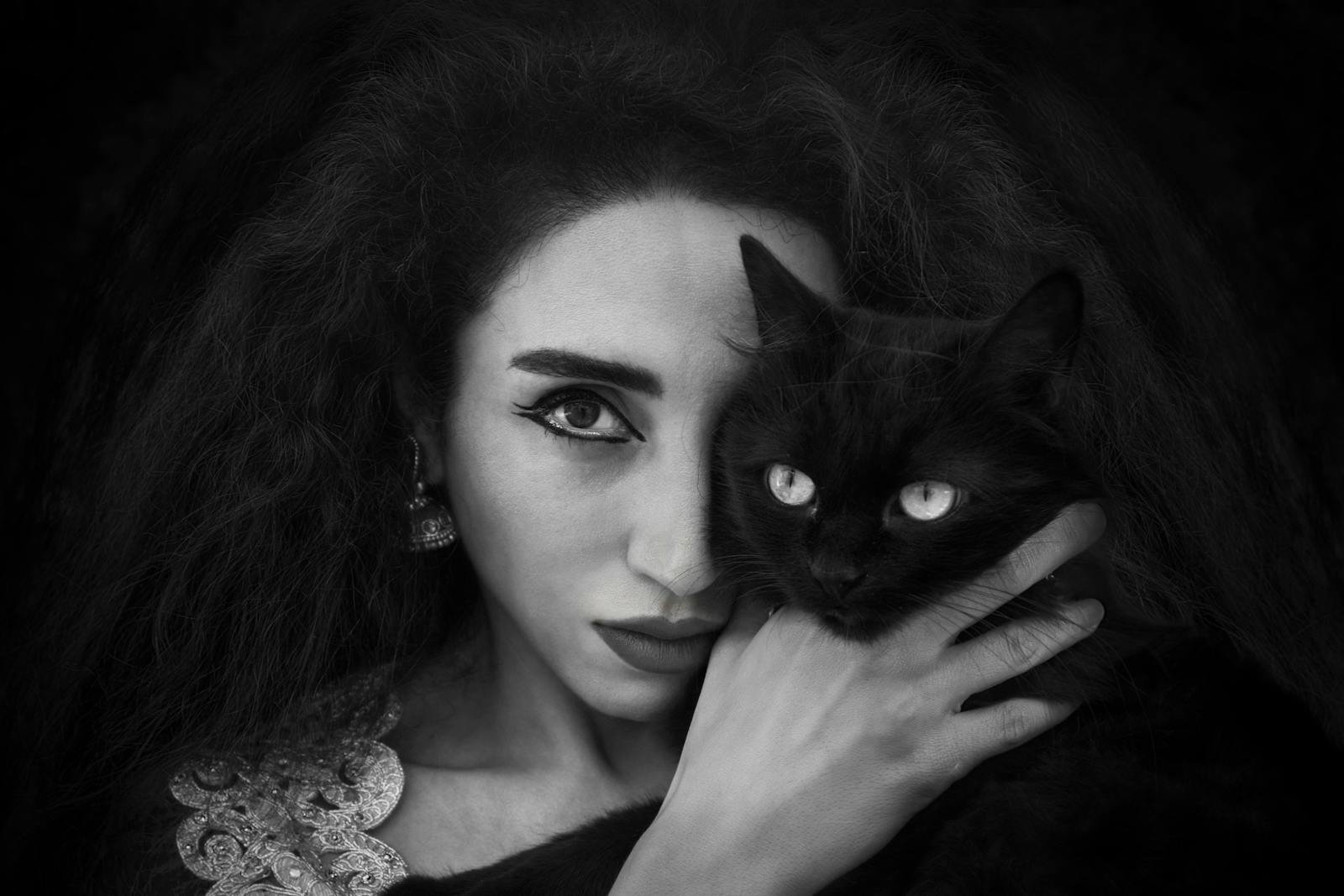 A striking black and white portrait of a woman holding a black cat, showcasing elegance and mystery.