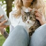 A young woman enjoying the outdoors with her tabby cat and smartphone, capturing the moment.