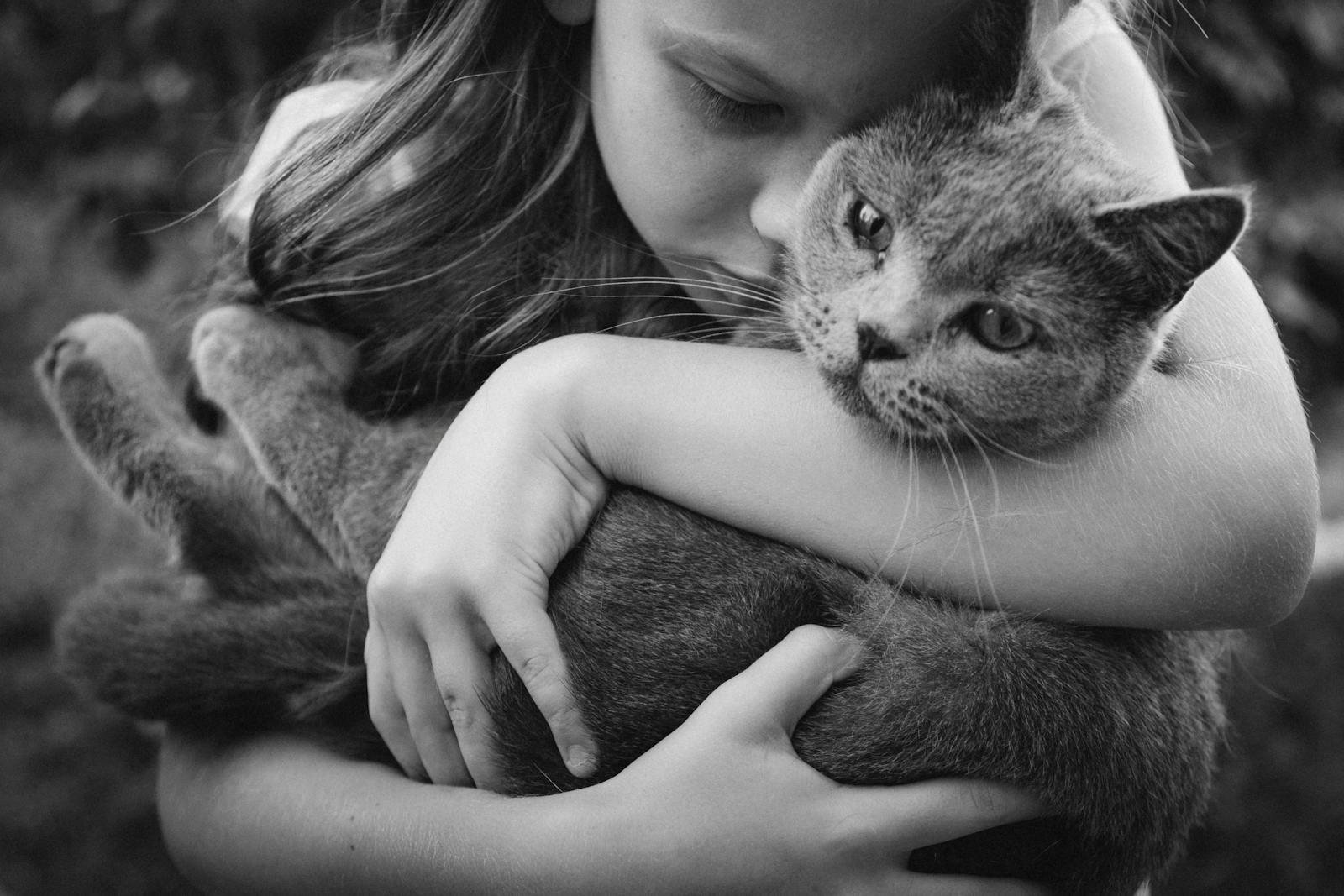 A young girl lovingly embraces a cat in a black and white image, capturing warmth.