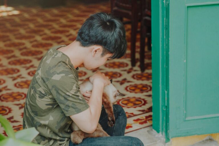 A young boy in a camouflage shirt lovingly cuddles a cat near a green doorway indoors.