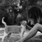 A black and white photo of a woman lovingly petting a cat outdoors, showcasing a calm moment.