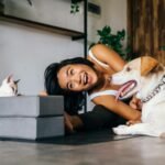 Smiling woman practicing yoga indoors with her dog and cat, embracing a healthy lifestyle.
