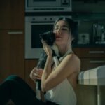 Woman enjoying a quiet moment cuddling her kitten in a warmly lit kitchen.