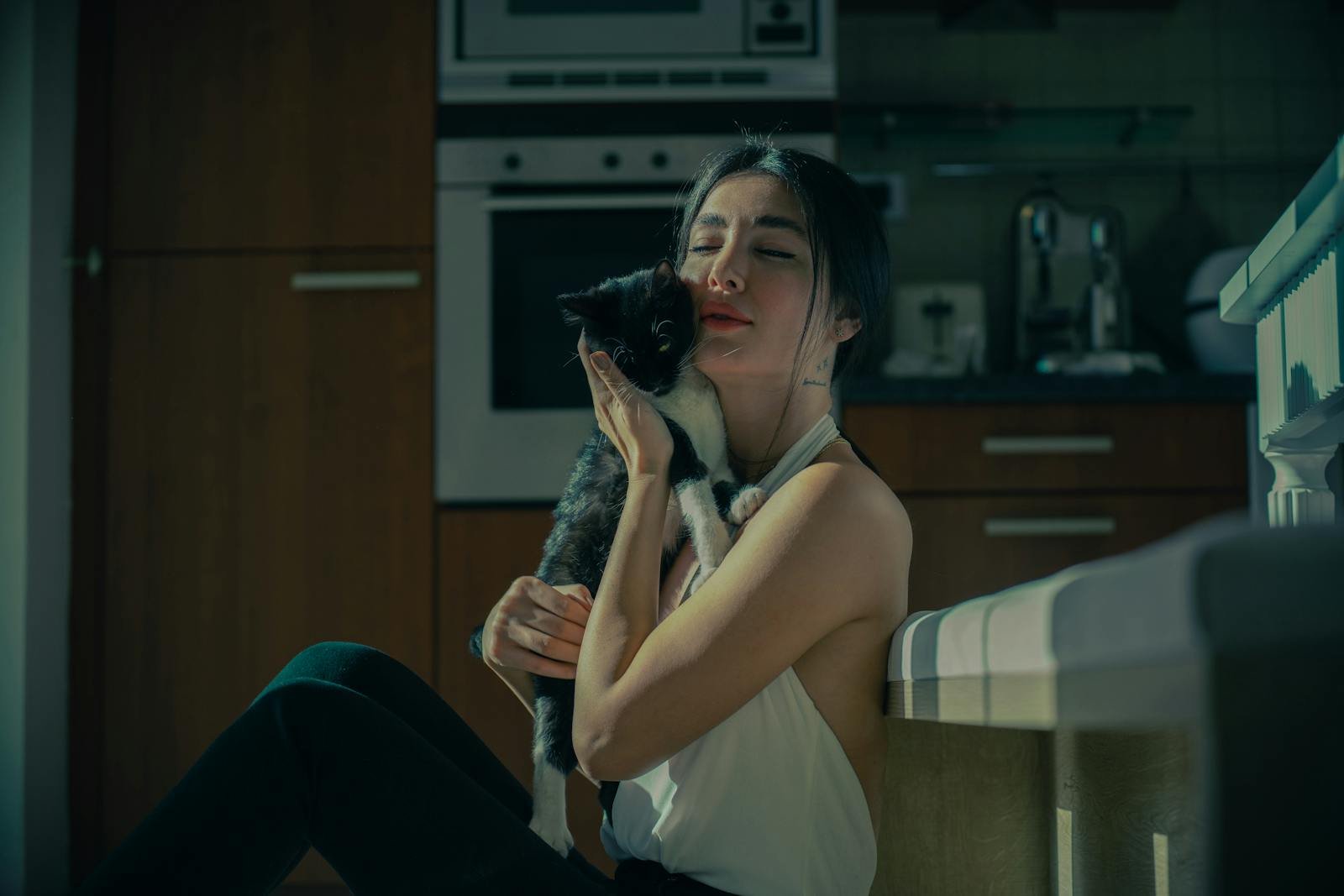 Woman enjoying a quiet moment cuddling her kitten in a warmly lit kitchen.