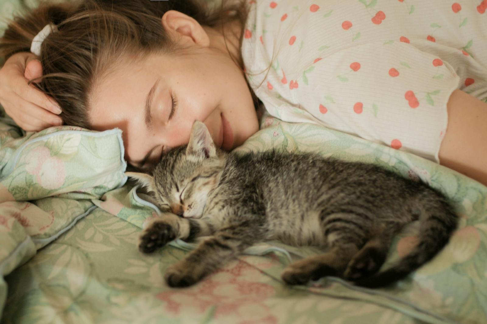 Woman and tabby kitten sleeping peacefully on floral bedding, embodying comfort and warmth.