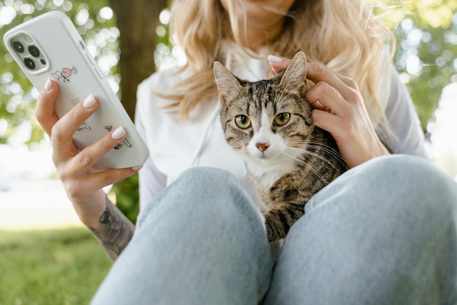 A young woman enjoying the outdoors with her tabby cat and smartphone, capturing the moment.