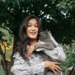 A joyful woman holding a cat in a vibrant garden captures a moment of playful affection.