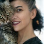 Close-up of a woman lovingly holding a fluffy tabby cat indoors.