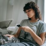 Woman sitting on a bed with a cat, using a smartphone, enjoying a calm, cozy moment indoors.