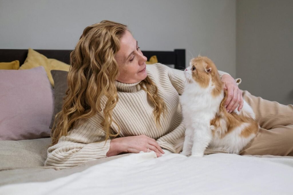 A woman lovingly holds a fluffy cat on a bed, capturing a moment of companionship indoors.