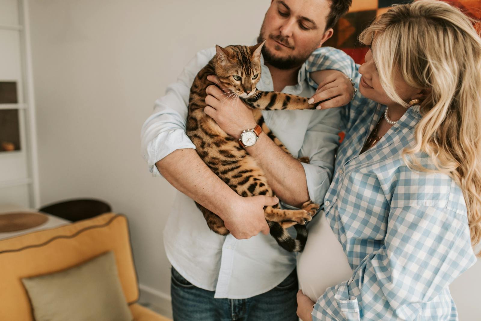 Pregnant couple happily interacting with their Bengal cat indoors.