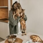 Pregnant woman hugs Bengal cat in cozy kitchen setting.