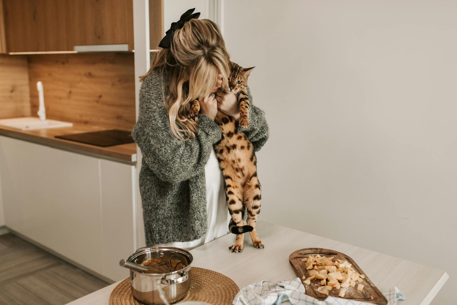 Pregnant woman hugs Bengal cat in cozy kitchen setting.
